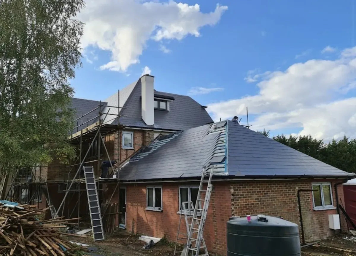 Roofers fitting a new dark grey slate roof on a large brick house extension with scaffolding